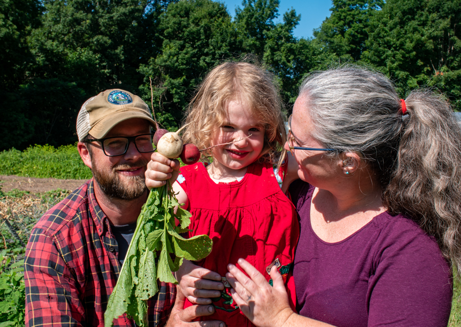 Two adults hug their child in a field