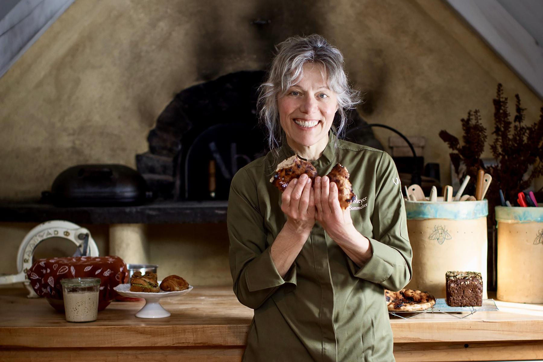Heike Meyer of Brot Bakehouse stands before her baking table and earthen oven holding sourdough bread