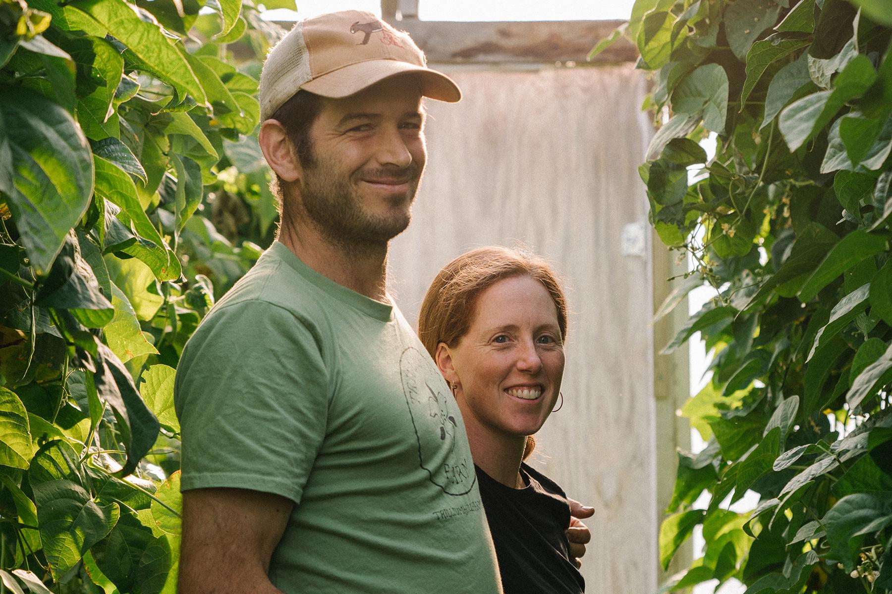 Farmers James and Sara of Trillium Hill farm standing between tall rows of lush organic bean vines in their high tunnel