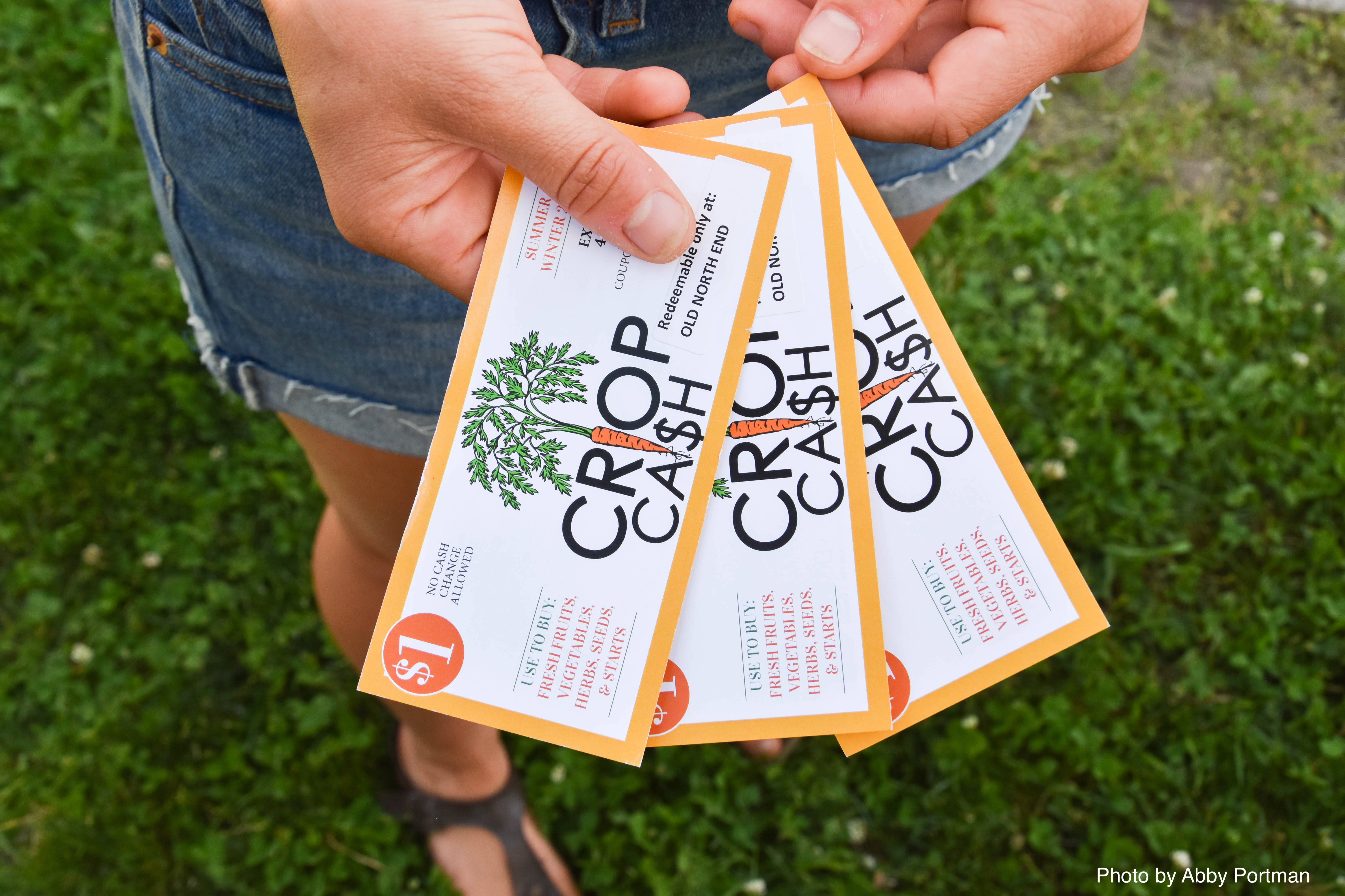 A fan of three $1 Crop Cash Coupons held by a farmers market shopper