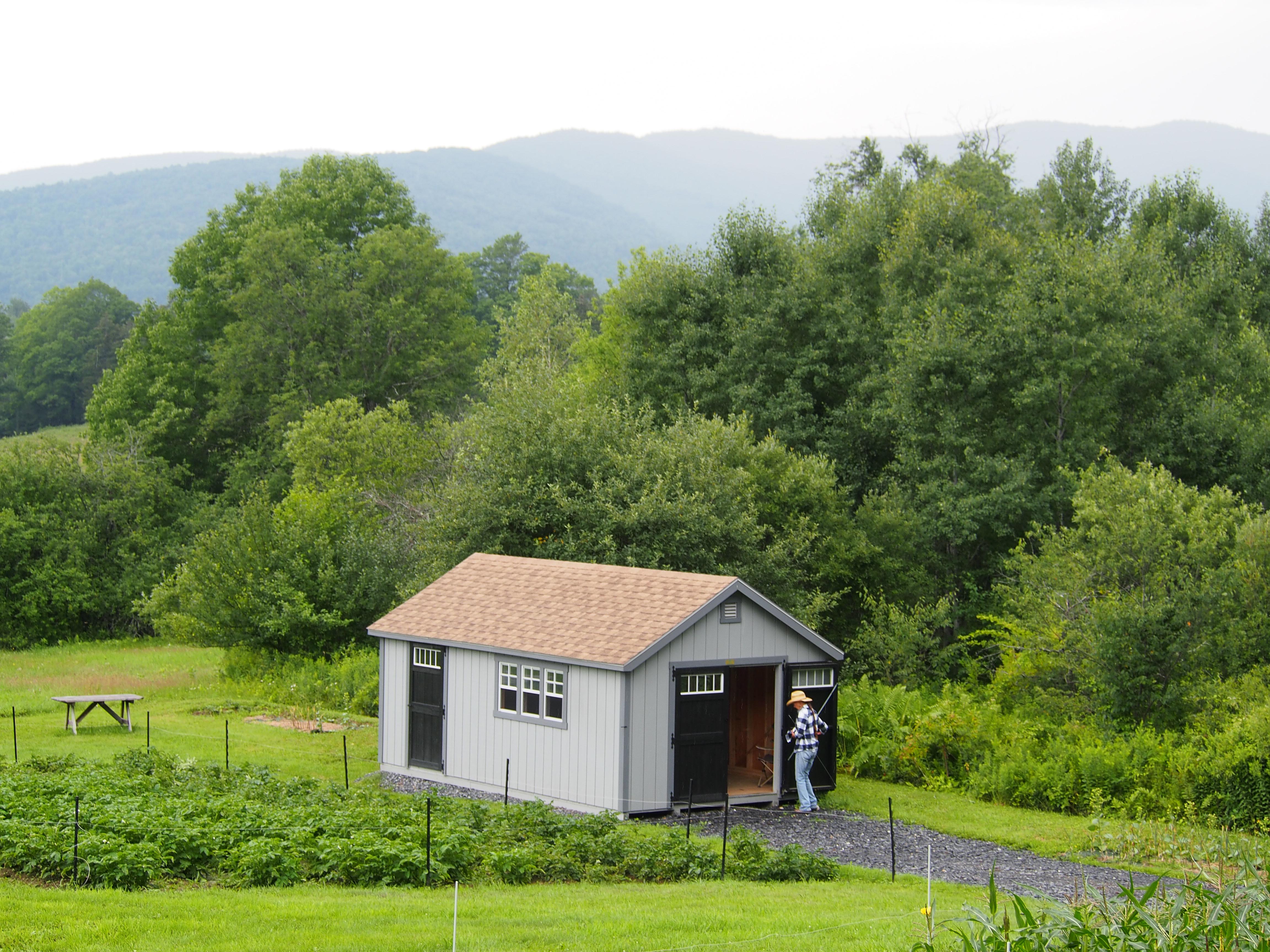 A farmer is seen from afar, approaching a small outbuilding. 