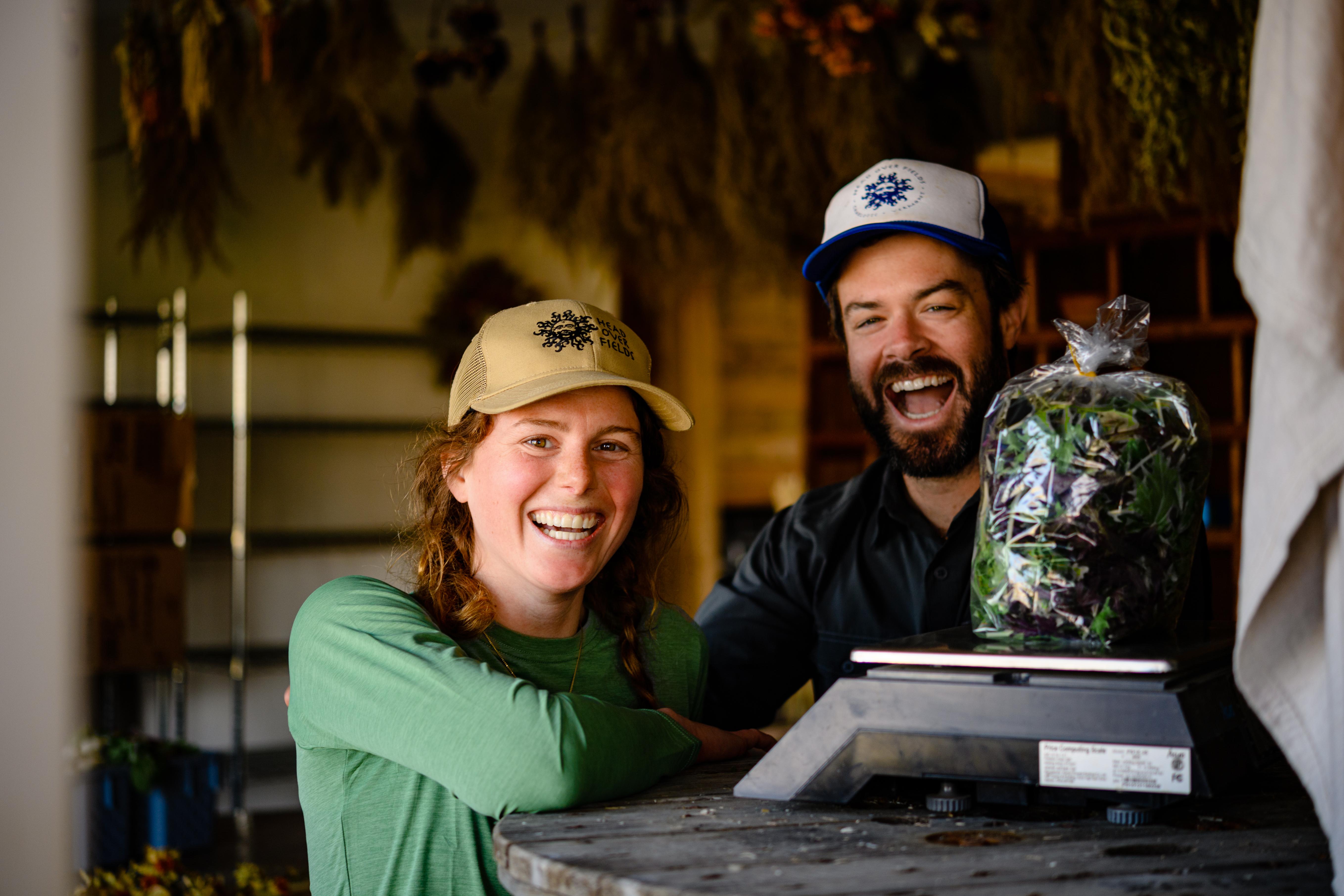 Farmers Katie Rose and Brian of Head Over Fields Farm smiling at their farmstand