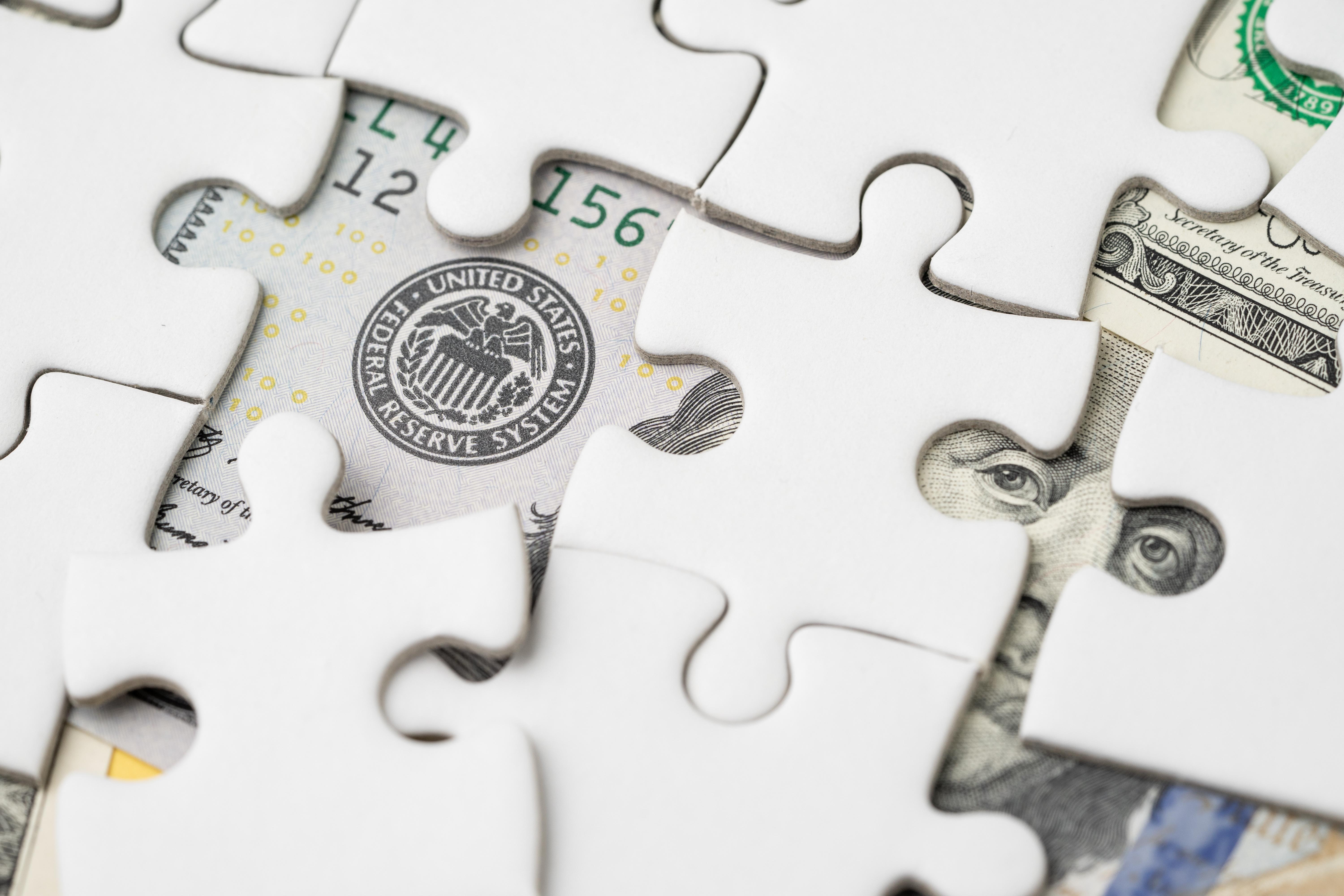 white puzzle pieces partially snapped together over a backdrop of US currency