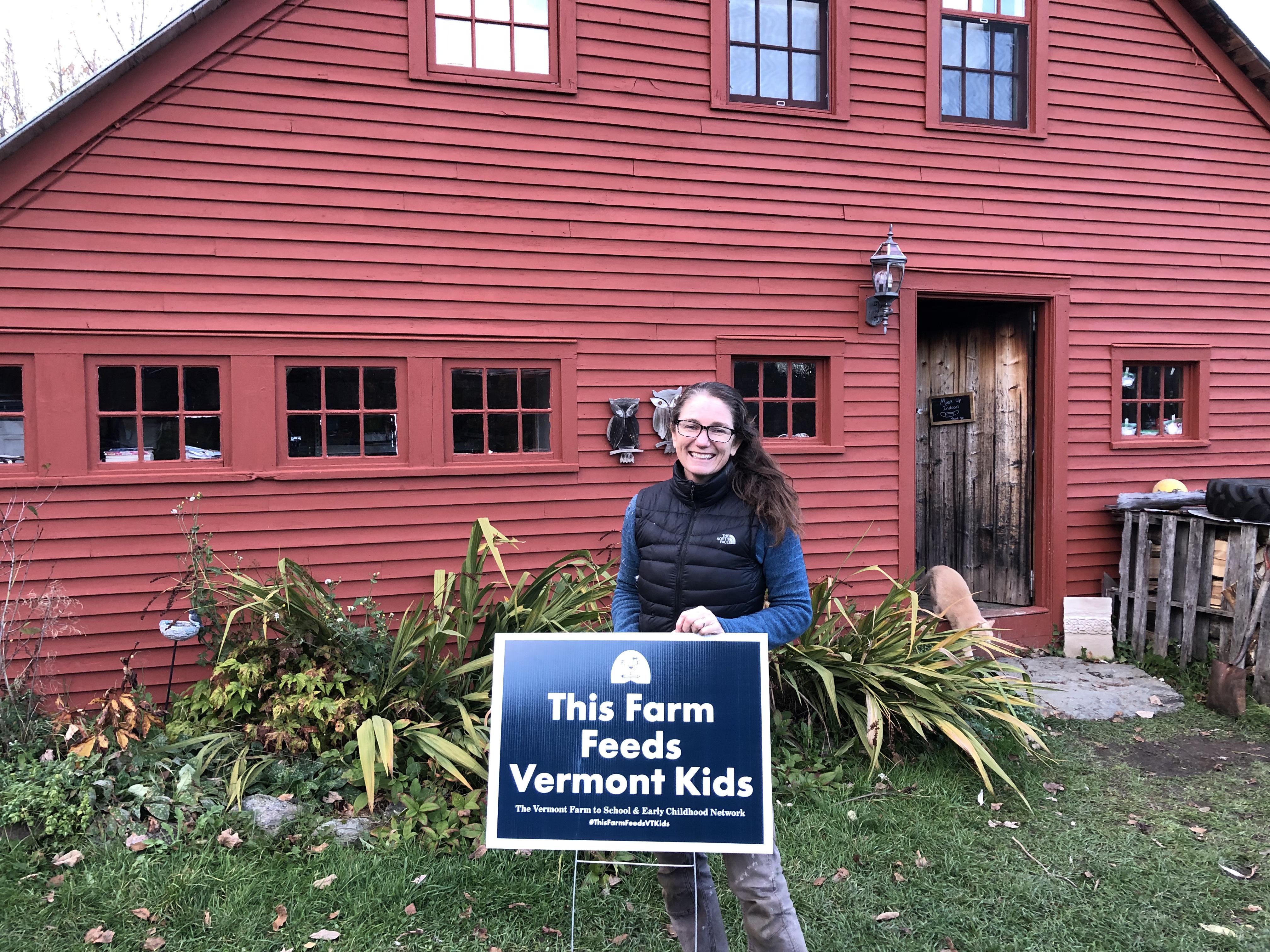 Misse Axelrod of the Farm & Forest Day School at Drift Farmstead stands proudly with a sign reading "This Farm Feeds Vermont Kids"