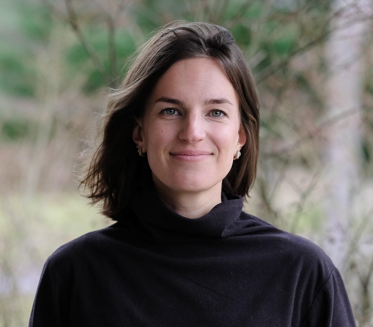 Lindsey Brand headshot. White woman with brown hair stands outside in front of a tree.