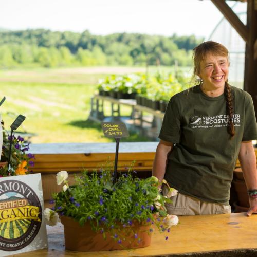 A person stands behind a counter on a farm displaying the Vermont Organic Farmers seal.