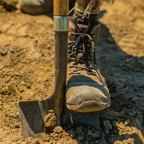 A farmer's boot stomps a shovel into the soil