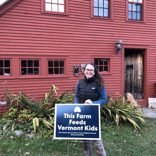 Misse Axelrod of the Farm & Forest Day School at Drift Farmstead stands proudly with a sign reading "This Farm Feeds Vermont Kids"